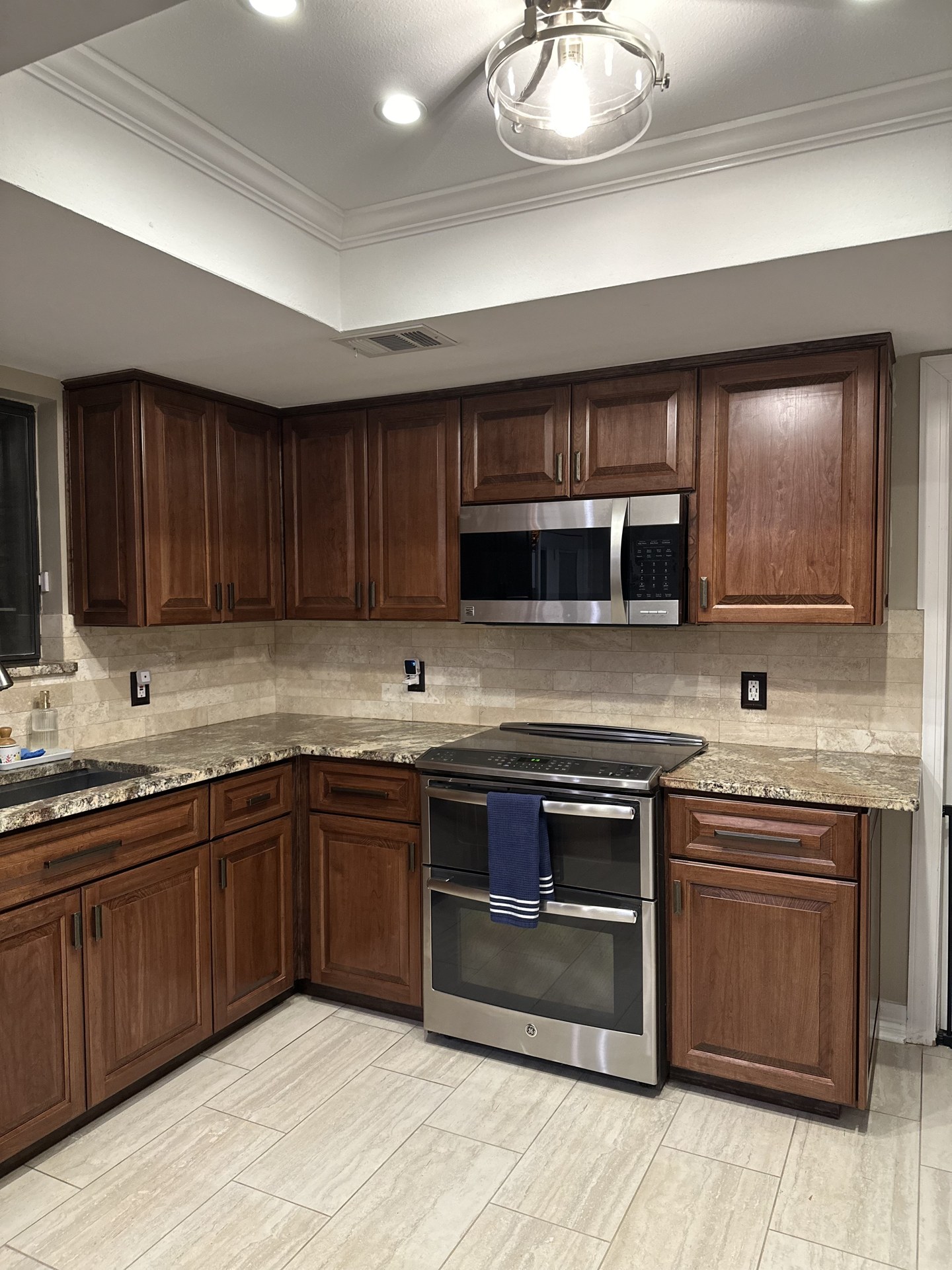 Refaced kitchen cabinets restained to a rich walnut brown with stone countertops and a tile backsplash in Round Rock