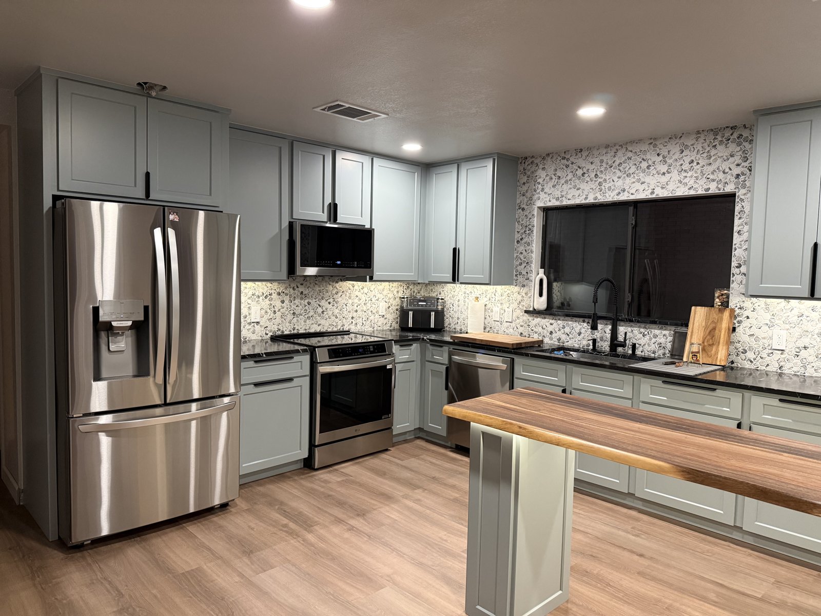 Remodeled kitchen with sage green shaker cabinets, dark countertops, pebble tile backsplash, and a walnut-top island in Round Rock